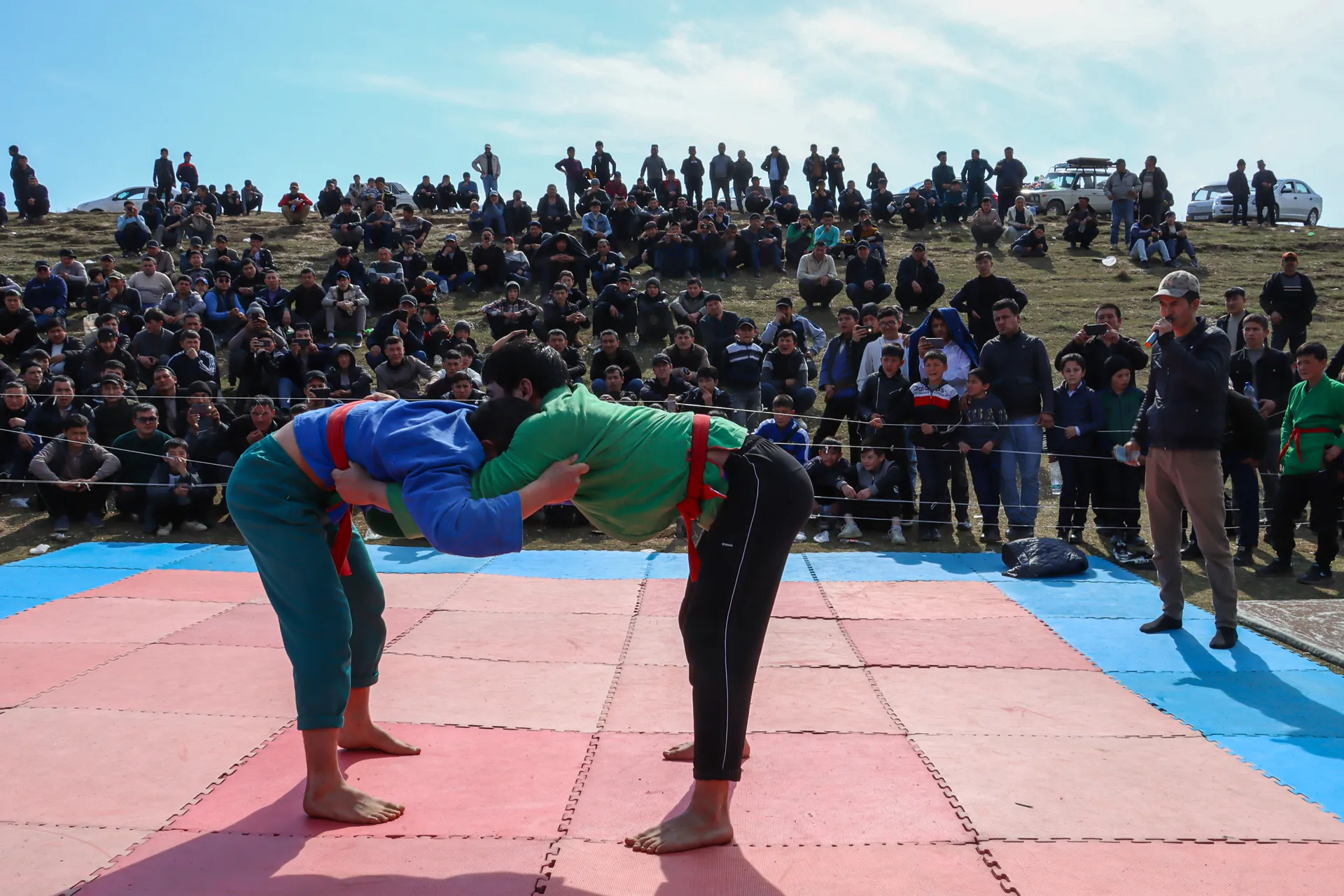 A kurash bout on a mat in the open air, surrounded by the whole village — wrestling is part of every big celebration.