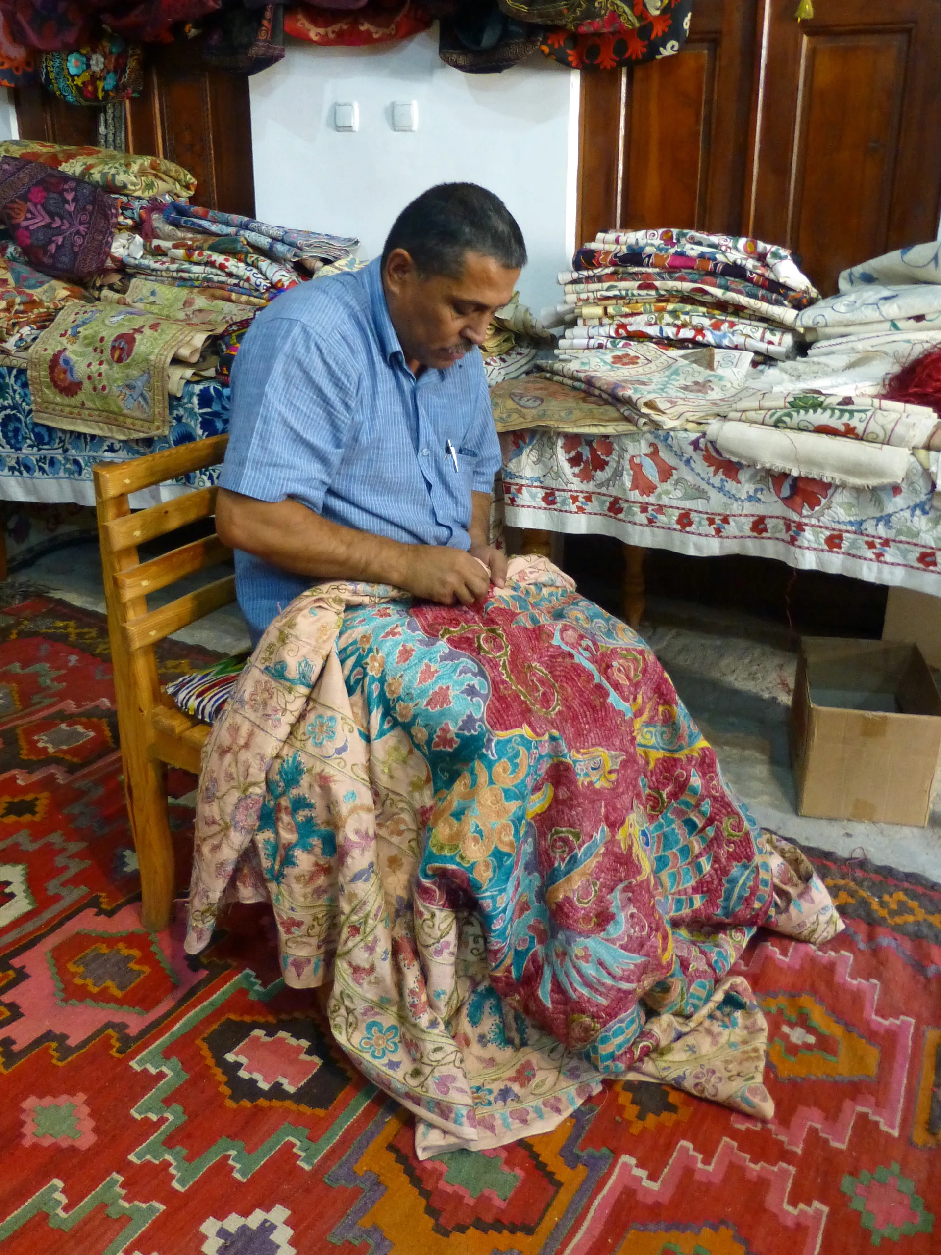 A craftsman working a suzani panel by hand in a Bukhara workshop; a large piece can take months.