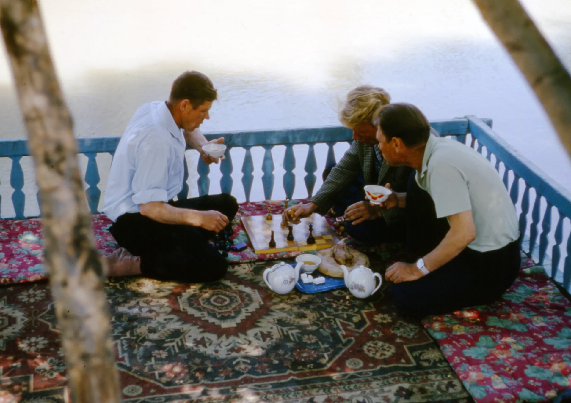 Men sharing bread, tea and dishes on a carpeted tapchan platform beside the water in a Tashkent choyxona.